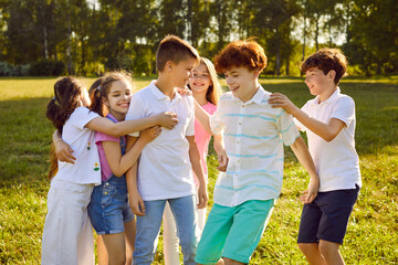Portrait of happy smiling teenage children friends standing on the green grass together in the park outdoors hugging and having fun in nature. Kids summer camp and holidays concept.