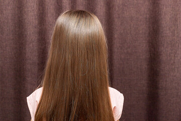 A portrait of a two years old little girl turn back to show her braided hair tied with ribbons.