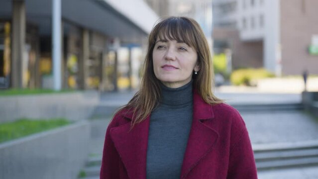 An attractive middle-aged Caucasian woman looks around in thought as she walks in an urban area