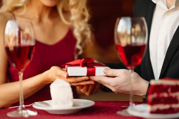 A young couple in love exchanges gifts for Valentine's Day in a cafe at the table. Handsome man and...