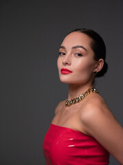 Portrait of young beautiful brunette woman in red latex dress with chain and red lipstick.