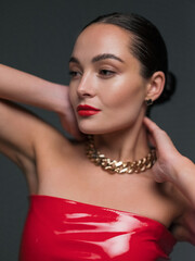 Portrait of young beautiful brunette woman in red latex dress with chain and red lipstick.