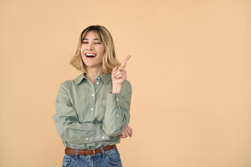 Obraz premium Happy pretty gen z blonde young woman, smiling student girl with short blond hair wearing shirt and jeans pointing aside presenting promotion laughing standing isolated on beige background. Copy space