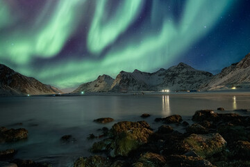 Aurora borealis with stars over mountain range on coastline