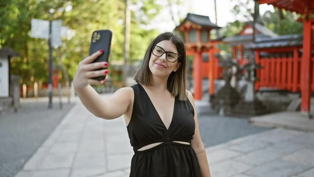 Vibrant selfie of a beautiful hispanic woman in glasses, all smiles capturing her fun-filled visit at the iconic fushimi inari-taisha temple, kyoto