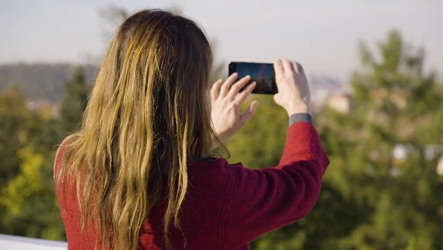 A woman takes pictures of a landscape and cityscape with a smartphone - rear view