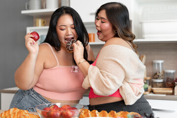 Happy Asia plus size woman eating donut with friend in kitchen at home