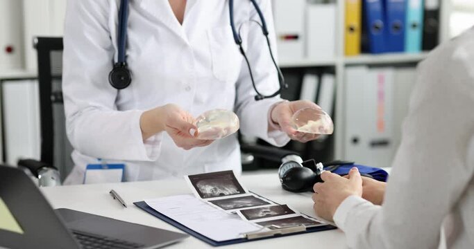 Doctor shows silicone implants for breast augmentation to patient in clinic closeup. Cosmetic surgery and breast augmentation concept