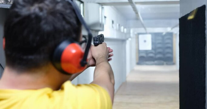 Rear view of man aiming gun at target in shooting range. Pistol shooting training concept