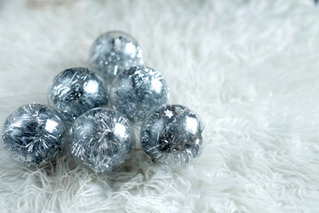 Christmas transparent balls with silver glitter filling on a white fur background with free space..