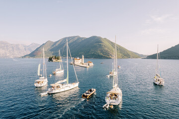 Motor yacht and sailboats sail along the Bay of Kotor to the island of Gospa od Skrpjela. Montenegro. Drone - obrazy, fototapety, plakaty