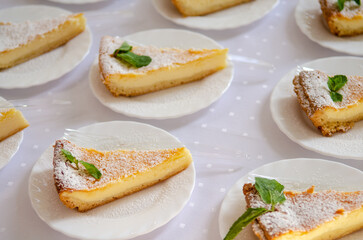 Triangular pieces of cheesecake with mint on white plates with forks, under the sun rays, catering at the event