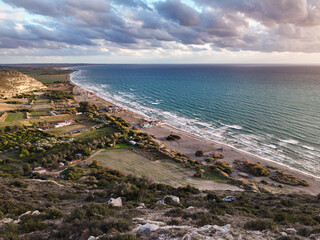 Obraz premium Sunset over Cyprus Kurion Beach, where golden hues dance on the serene Mediterranean waters, casting a tranquil glow. The sun kisses the horizon, painting the sky with warm shades of orange and purple