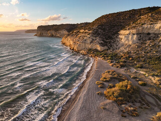 Sunset over Cyprus Kurion Beach, where golden hues dance on the serene Mediterranean waters, casting a tranquil glow. The sun kisses the horizon, painting the sky with warm shades of orange and purple