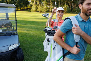 Naklejka premium Golfing Partners: Woman Selecting Club from Bag on Course