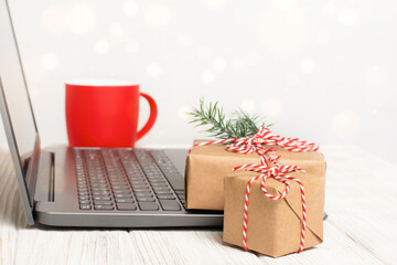 Obraz na płótnie Canvas Christmas gift boxes and cup near the laptop on white table. Working place with defocused lights and copy space. Online shopping or greeting concept