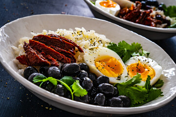 Boiled eggs with boiled white rice, sun dried tomatoes and green olives on wooden table
