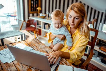 Mother holding baby using laptop at home