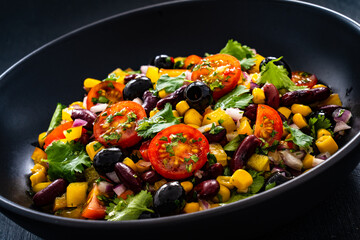 Mexican style salad - red beans, black olives, corn, yellow pepper, onion and tomatoes on wooden table