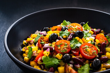 Mexican style salad - red beans, black olives, corn, yellow pepper, onion and tomatoes on wooden table