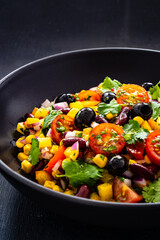 Mexican style salad - red beans, black olives, corn, yellow pepper, onion and tomatoes on wooden table