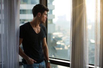 A man standing in front of a window looking out at the city
