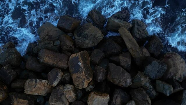 Panorama from above of the waves crashing on the rocks. Bright light blue colour.