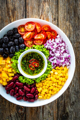 Mexican style salad - red beans, black olives, corn, yellow pepper, onion and tomatoes on wooden table