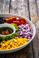 Mexican style salad - red beans, black olives, corn, yellow pepper, onion and tomatoes on wooden table