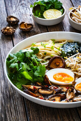 Asian style soup. Broth with chow mein noodles, boiled eggs, shiitake mushrooms, cilantro and mung sprouts on wooden table

