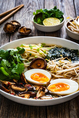 Asian style soup. Broth with chow mein noodles, boiled eggs, shiitake mushrooms, cilantro and mung sprouts on wooden table
