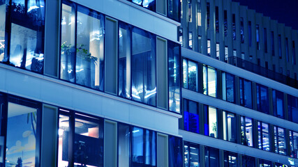 Fragment of the glass facade of a modern corporate building at night. Big glowing windows in modern...