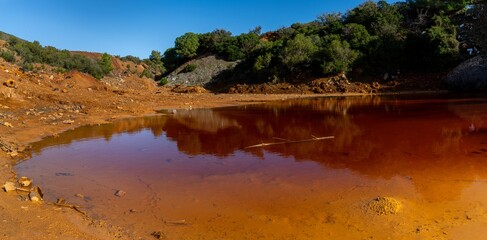 landscape view of a red waste water pond in an abandoned iron ore mine on Elba