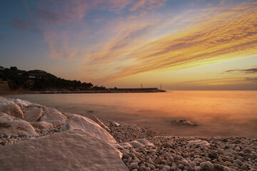 colourful sunrise over the white pebble beach and harbor of Mattinata in Italy