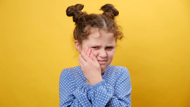 Dental problem. Close up portrait of little girl touching cheek, closing eyes with expression of terrible suffer from painful toothache, sensitive teeth, cavities, isolated on yellow background wall