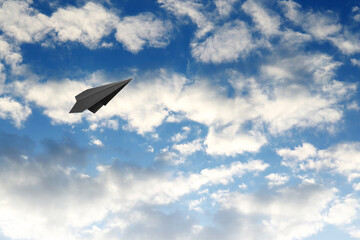 Fototapeta na wymiar Black paper plane flying in blue sky with clouds