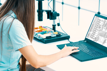 young woman in an electronics laboratory testing a printed circuit board using a microscope