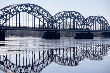 
A metal arched bridge across the river with the reflection of the bridge in the water in the form of an arch