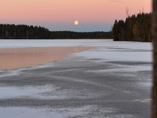 blue hour and moon rise on a lake in winter