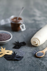 Concrete table with ingredients for baking, poppy seeds, dough in a roll, paste, decorated with DIY carnival masks. Festive sweet or salty pastries with poppy seeds. Preparation for Purim day