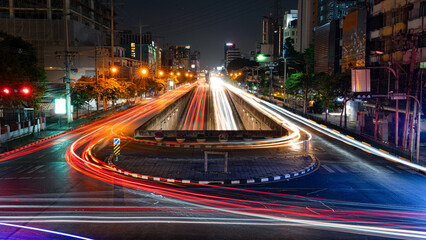 Time-lapse image of an elevated U-turn road. In the middle there were two parallel roads running in a straight line through the southern side. At night the city center There are tall buildings around.
