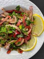 Salad with sliced lemon, onion, parsley, red pepper, sumach and tomatoes in porcelain bowl on dark background. Appetizer for Turkish pizza, pita pizza Lahmacun