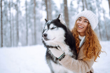 Cute woman spends time with her husky dog in the winter snowy forest. Happy pet dog owner having fun together outdoors. Fun concept. Lifestyle.