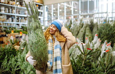 Happy woman in a bright hat buys a Christmas tree at the winter market. A young woman feels Christmas is approaching. Concept of holidays, traditions.