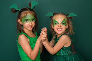 Two girlfriends dressed up as dragons with a pattern on their face are holding hands together. The...