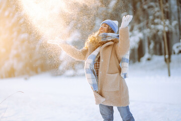 Young woman in warm clothes plays with snow on a sunny winter day. Happy female tourist enjoying a...