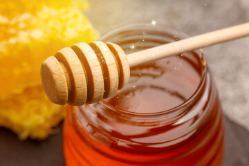 Natural honey in glass jar and wooden dipper under sunlight, closeup