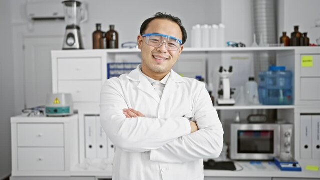 Smiling, confident young chinese man, a pro in science, at his lab station, standing with iconic arms crossed in the epicenter of research and medicine.