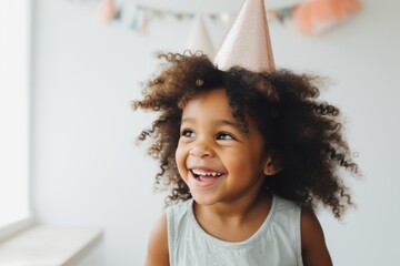Happy little girl in party hat on festive white wall background