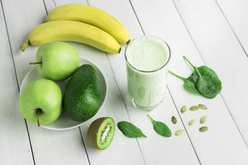 Green detox smoothie, blended vegetarian drink in a glass from spinach, apple, banana, kiwi, avocado and seeds on white wooden table, healthy eating concept